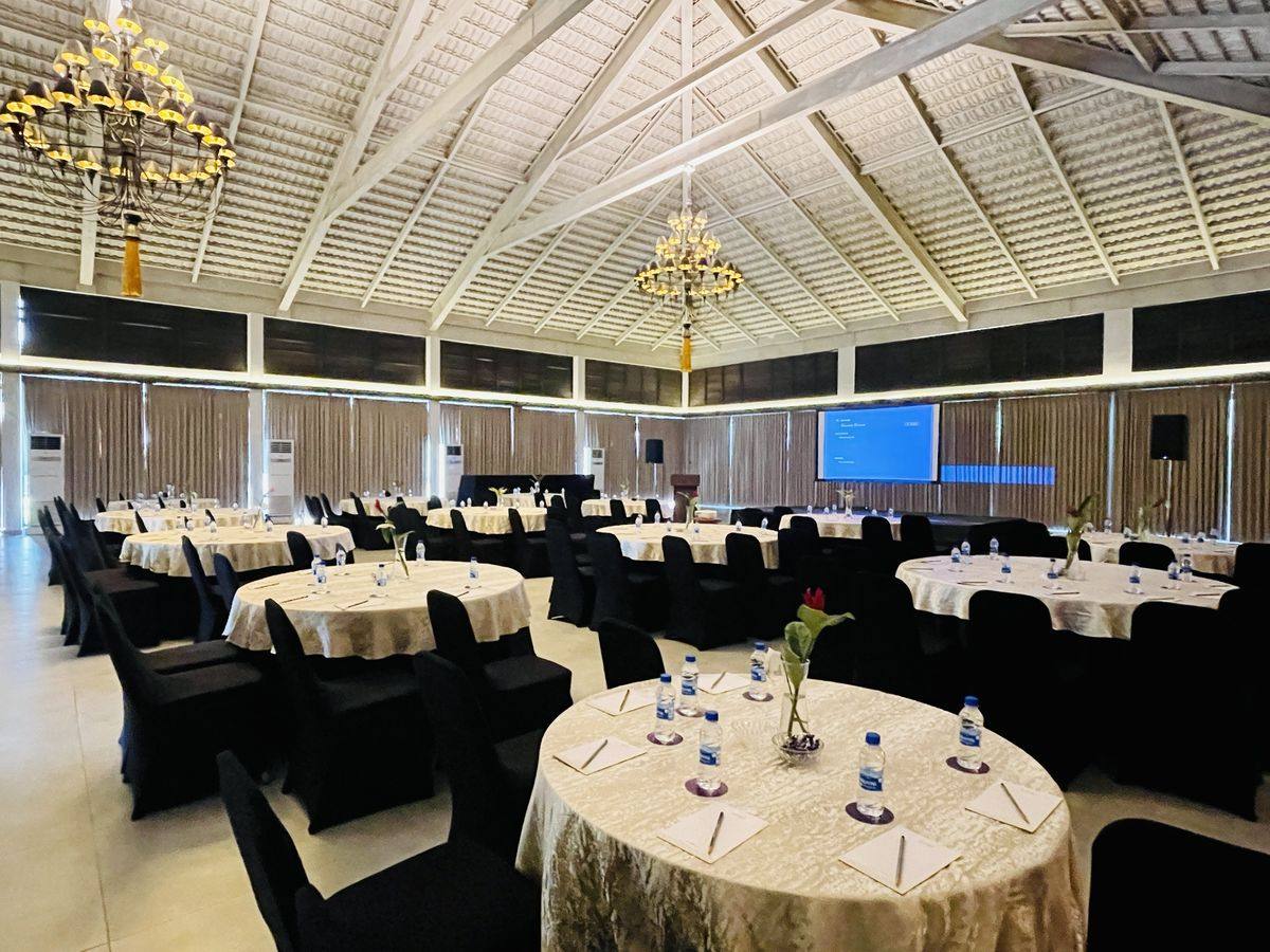A plenary hall set with round tables, stage and screen before the session